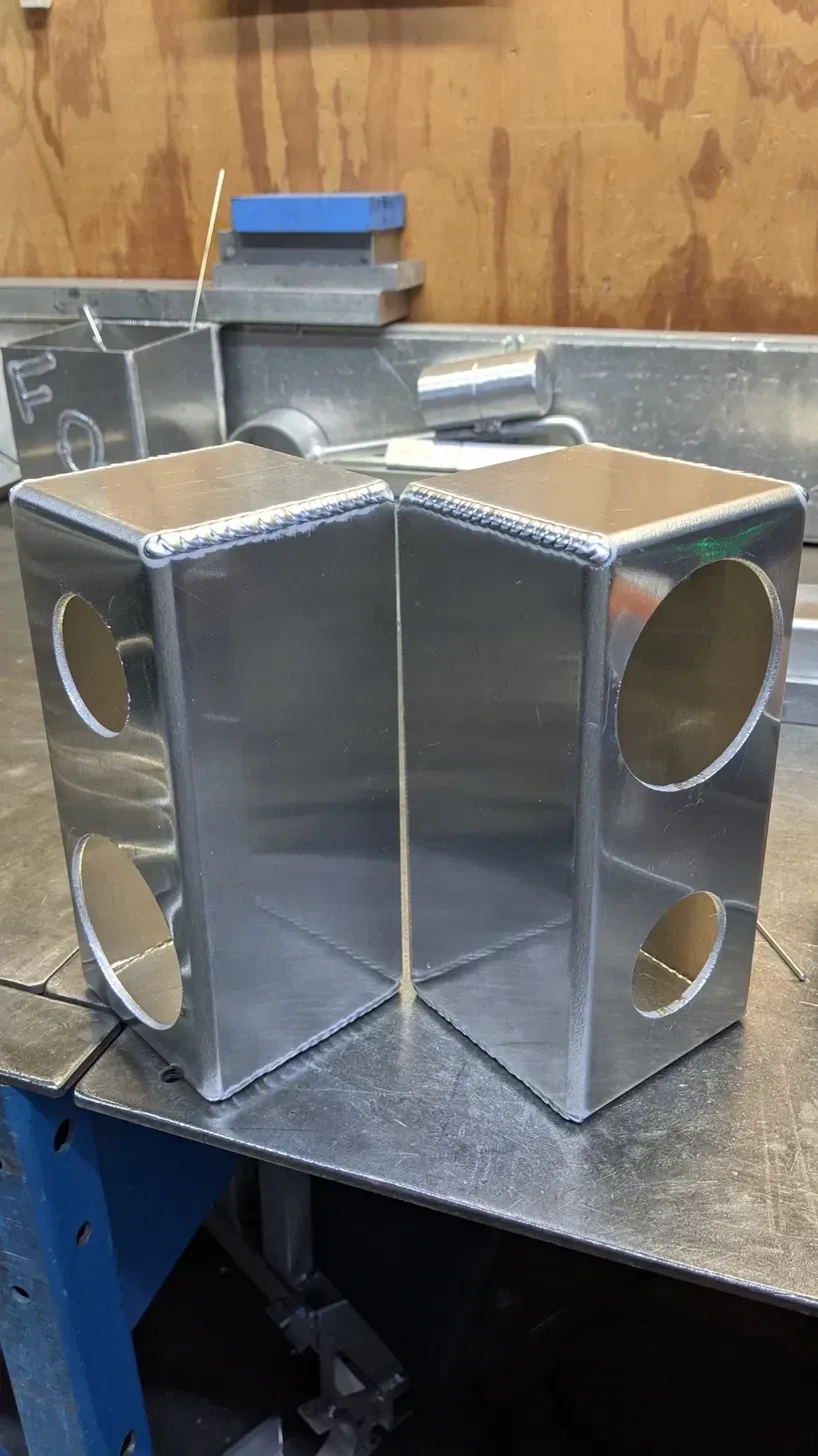 Pair of TIG-welded aluminum end tank caps on a fabrication table