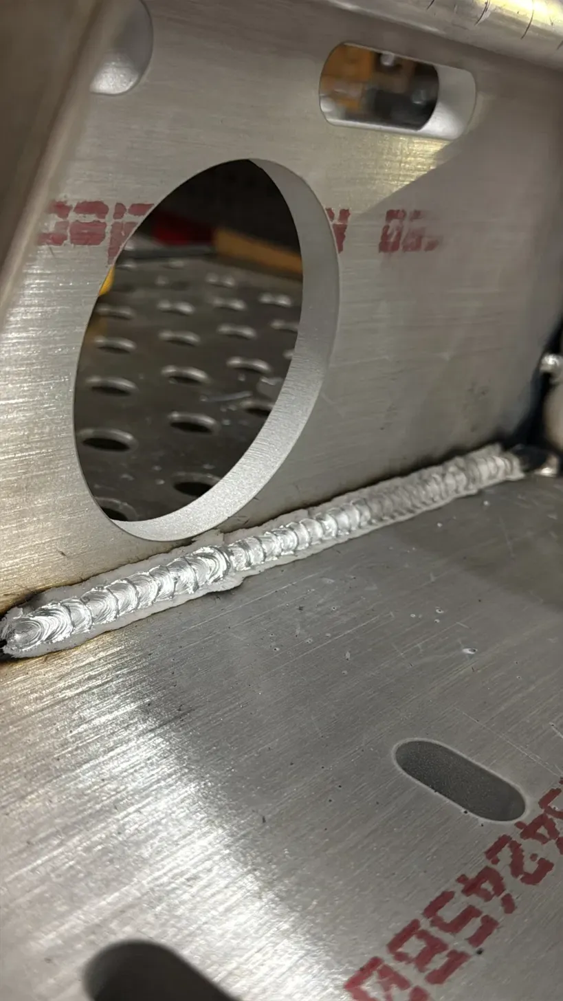 Close-up of a clean stacked-dime TIG weld on an aluminum bracket