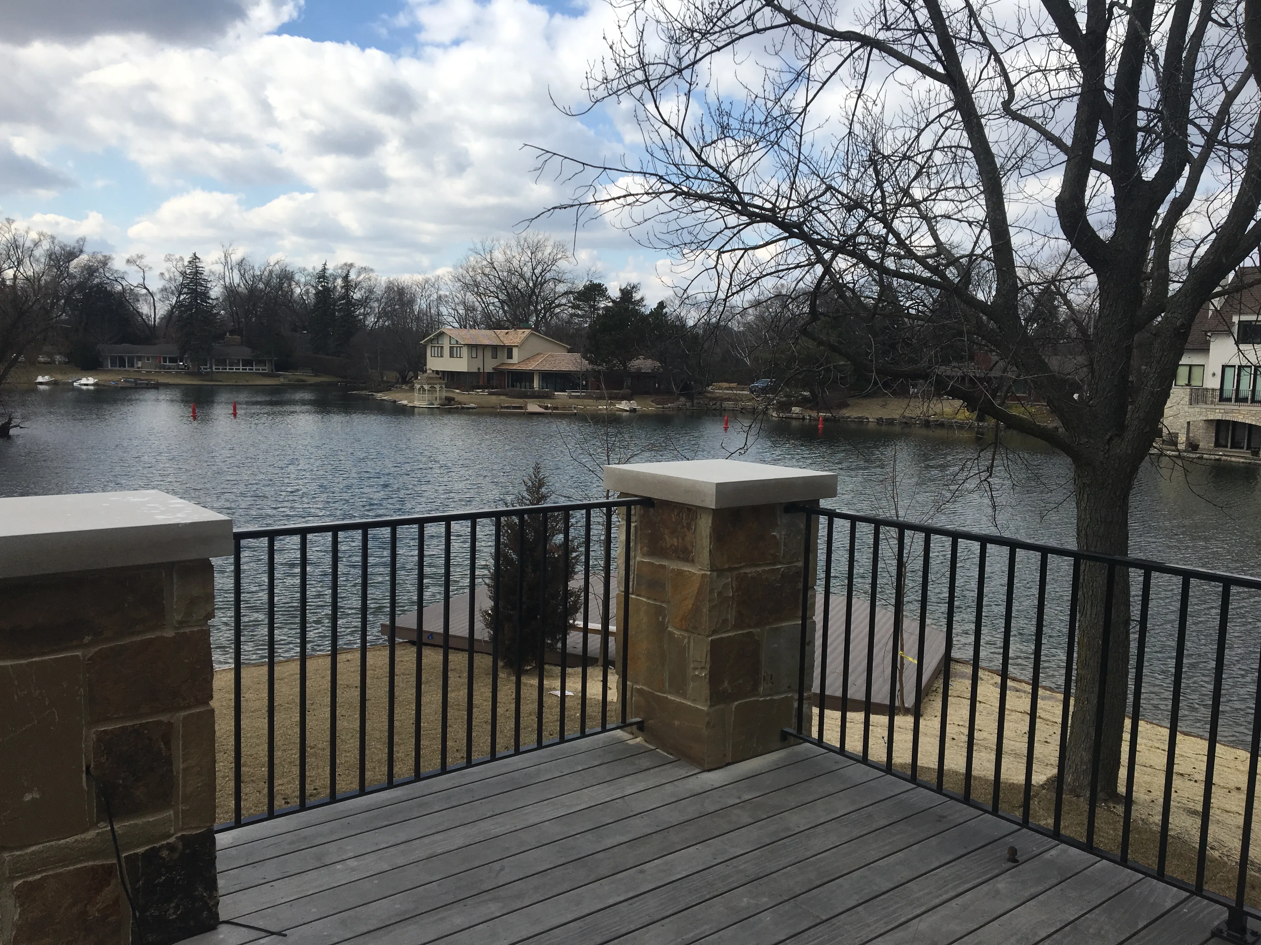 Custom black metal railing fitted between stone pillars on a lakeside deck